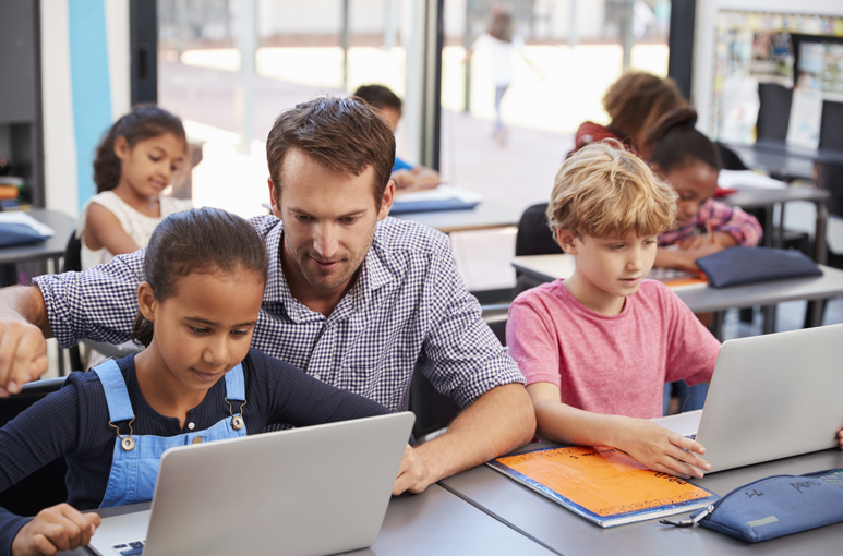 photo enseignant du primaire avec des élèves en classe travaillant sur ordinateur
